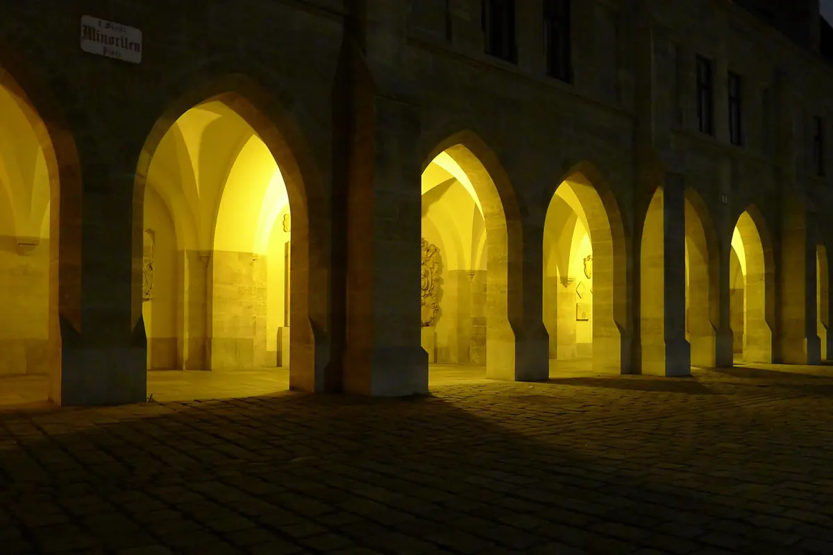 The arcade beside the church at night, with a row of pointed stone arches lit from inside in warm yellow light.