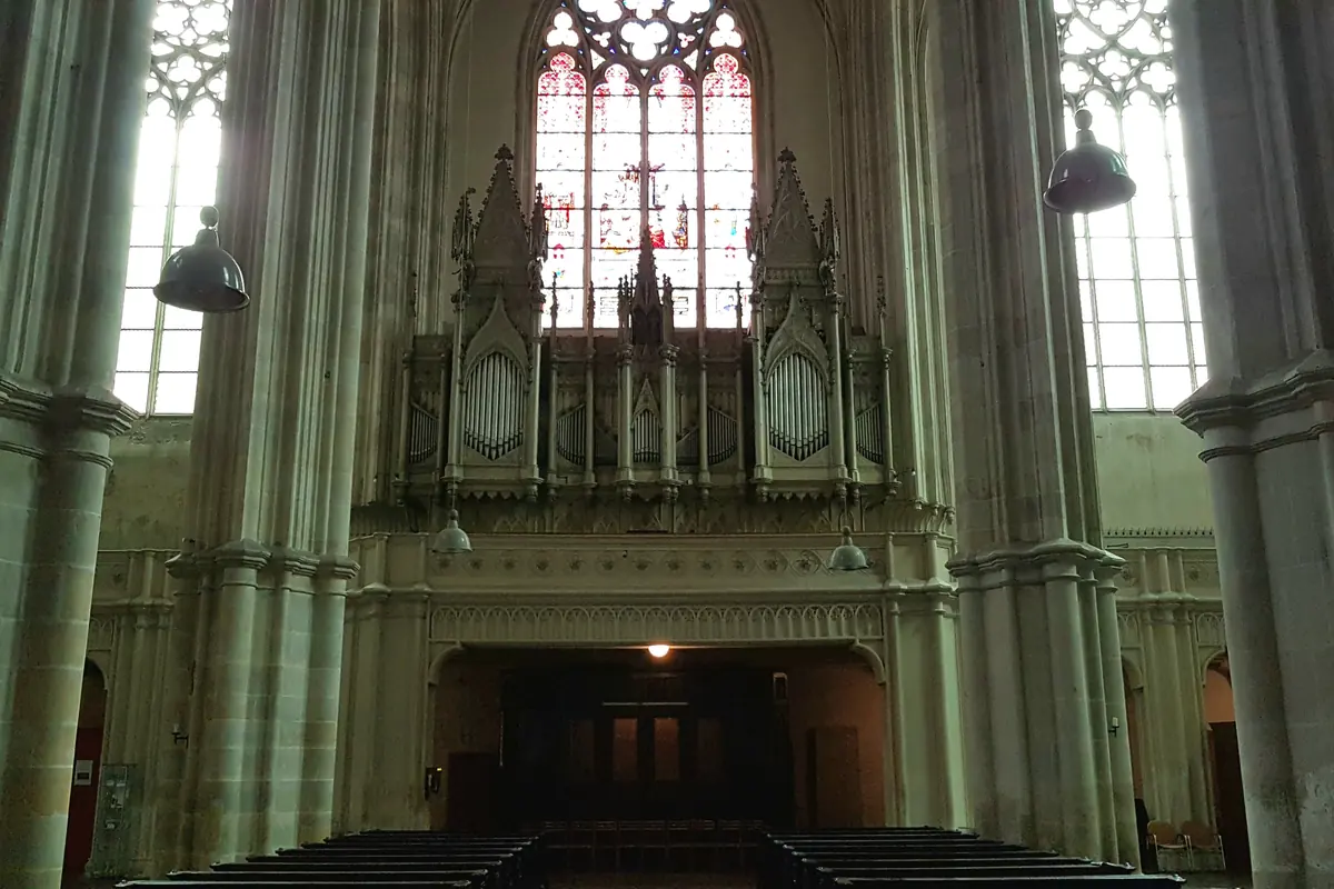 An organ case under a tall pointed window at the west end of the church, between pale-green stone piers.