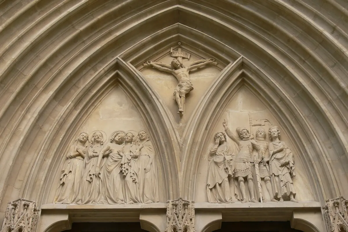 The carved tympanum of the main portal, with a crucified Christ at the top and groups of mourning figures in two pointed arches below.