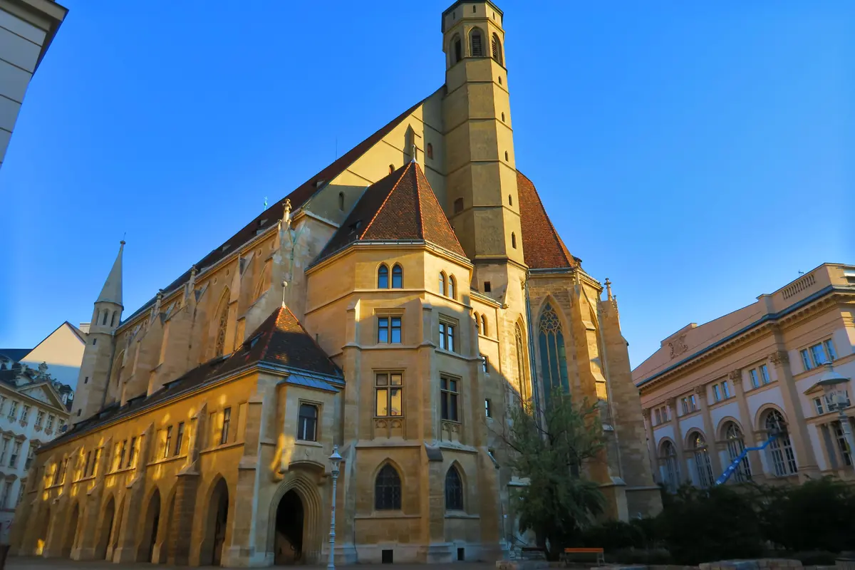 The Gothic church in low evening light, with a tall roof, an octagonal tower and a red-tiled gable beside a baroque palace.