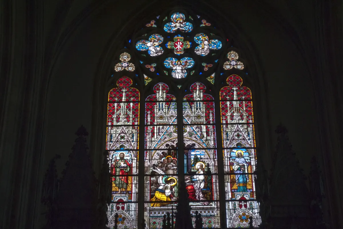 A tall pointed stained-glass window with a rose window of coloured glass above three lancets, in a dark stone wall.